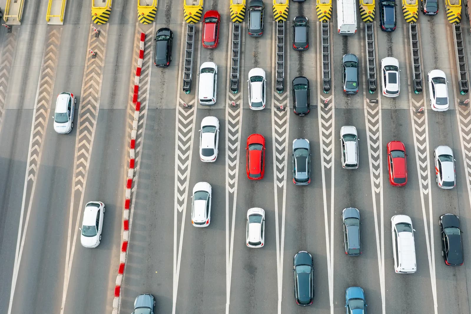 Rows of cars lined up in lanes at a highway toll plaza, seen from directly above