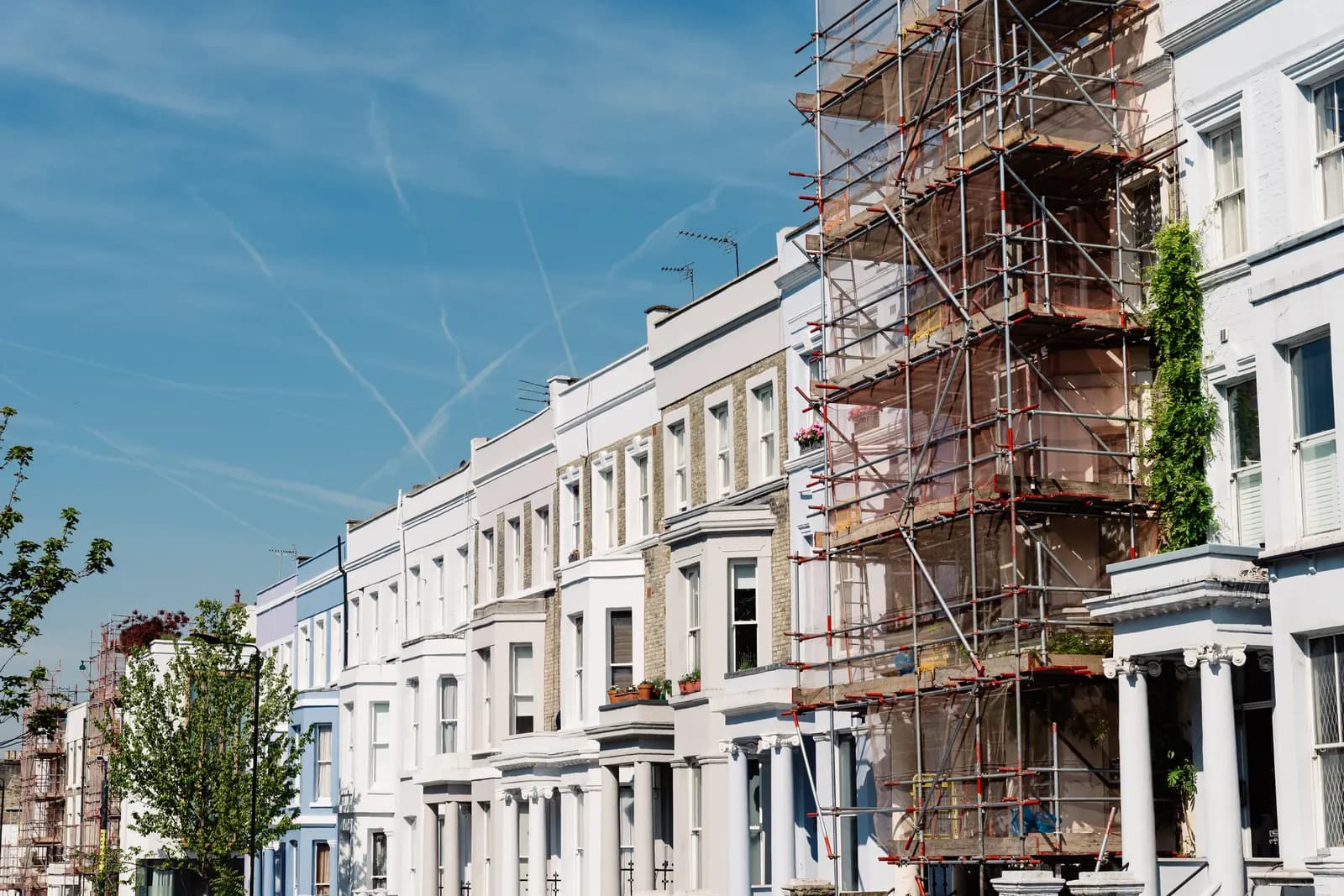 A row of pale terraced townhouses under a blue sky, one of them wrapped in scaffolding for renovation